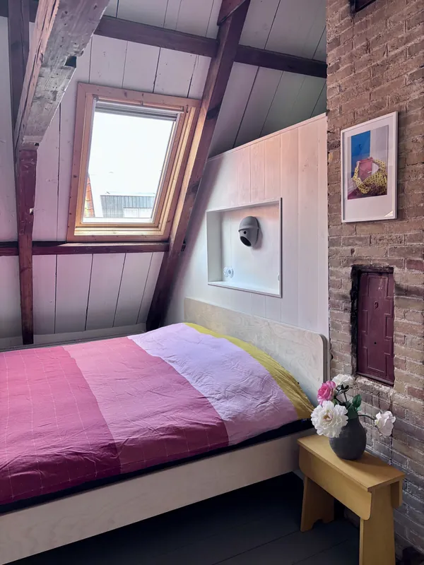 Slaapkamer in de loft met een roze bed onder het dakraam