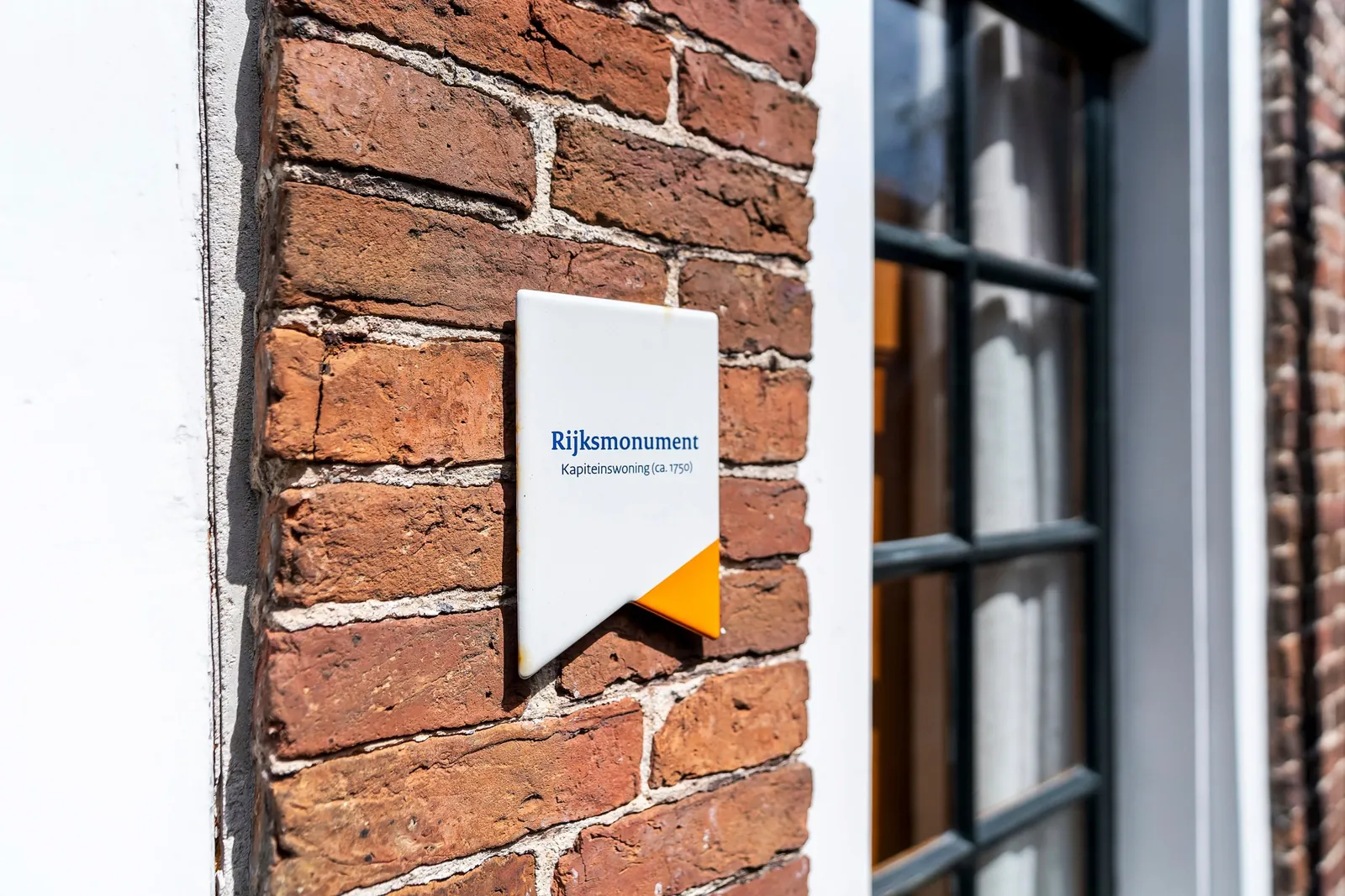 Rijksmonument-schildje naast het raam in de bakstenen gevel