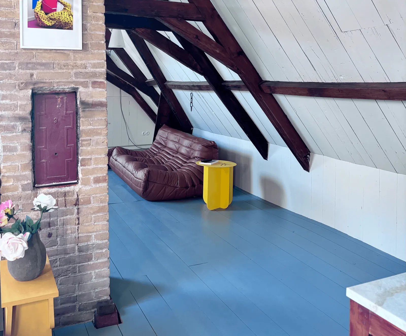 De loft met een bruine bank onder de dakbalken en een blauwe vloer