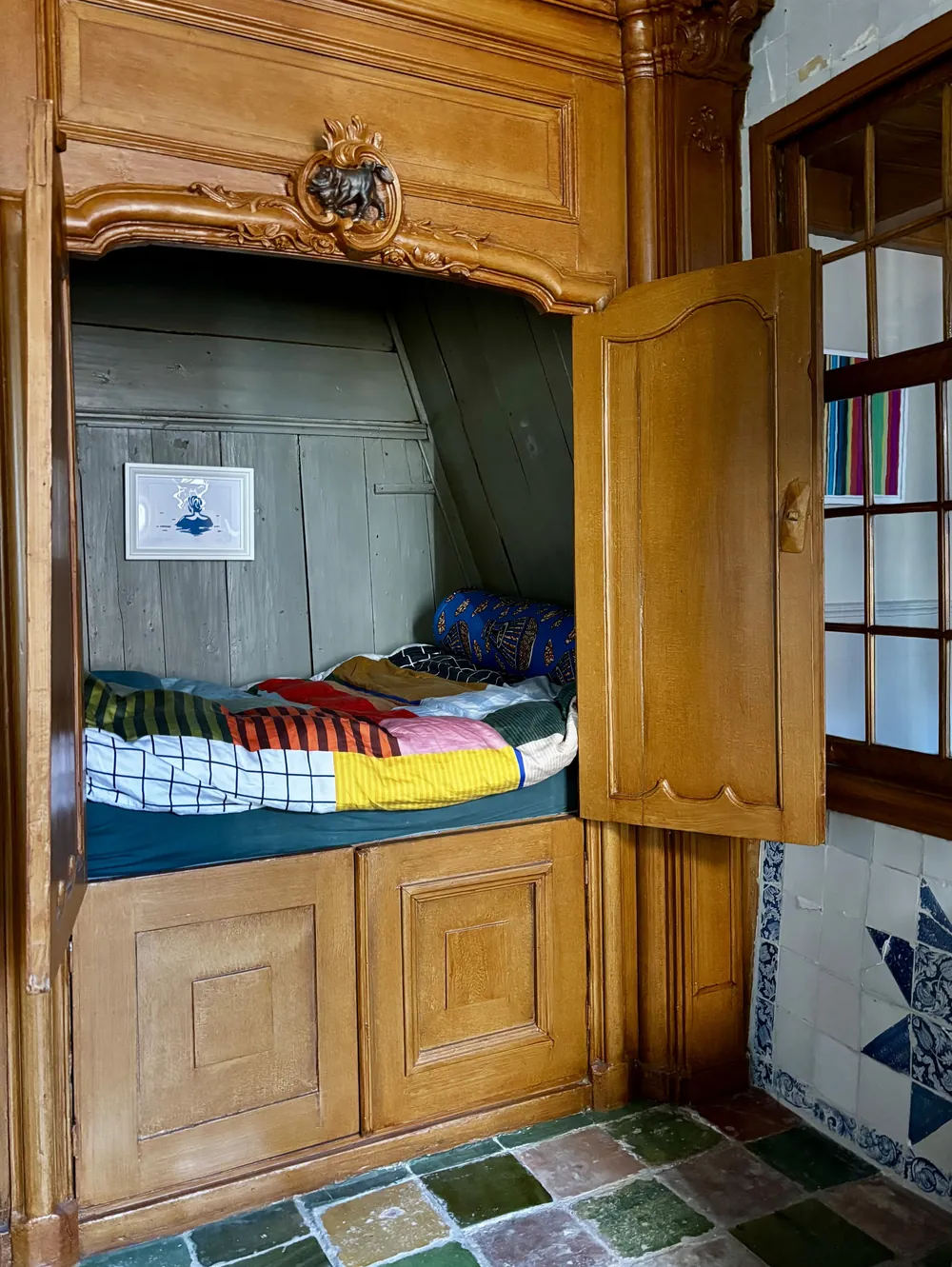 Originele bedstede met houtsnijwerk en een kleurrijk dekbed