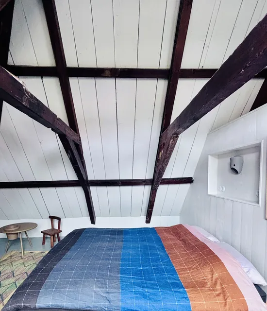 Bed in de loft onder witte planken en donkere balken